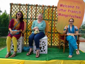 Three women sitting in front of UP Mango festival sign